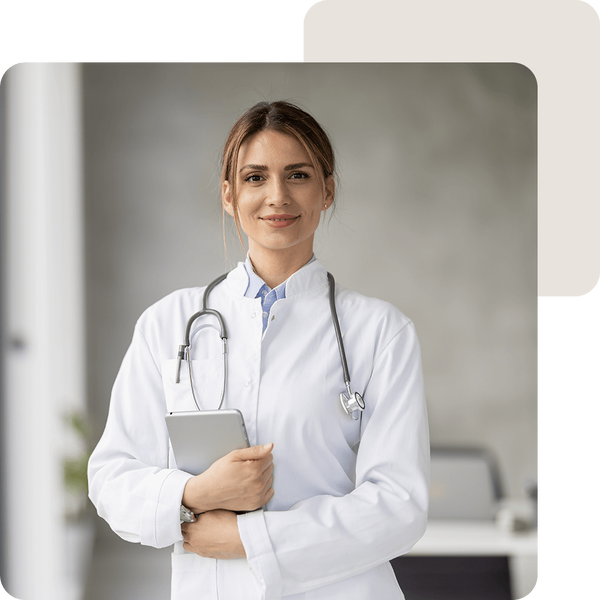 Ärztin in einer Klinik mit Stethoskop und Tablet blickt lächelnd n die Kamera