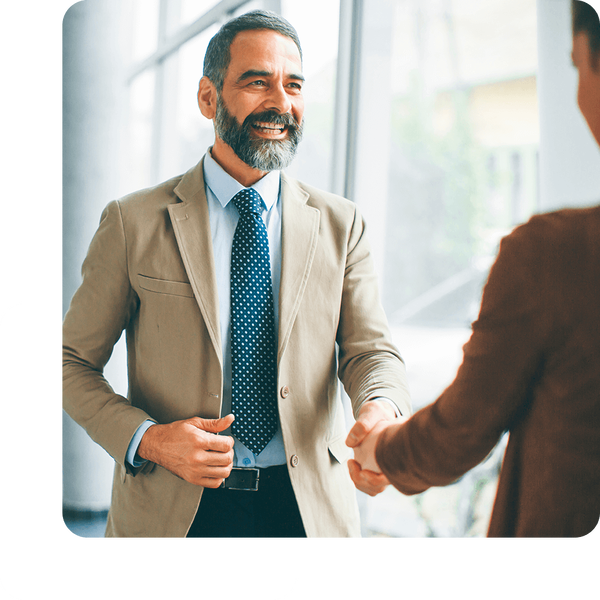 Zwei Männer im Sakko geben sich die Hände; der rechte Mann ist im Anschnitt von Hinten zu sehen.